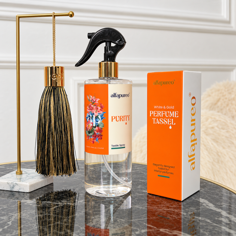 Purity Textile Spray s čiernozlatým parfumovým strapcom a krabičkou na mramorovom stolíku.