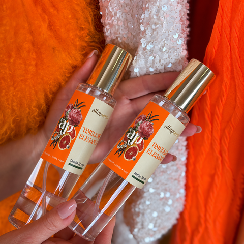 Nahaufnahme von zwei Timeless Elegance Textil- und Raumparfums von AlfaPureo in Händen vor orangefarbenem Fell und Pailletten